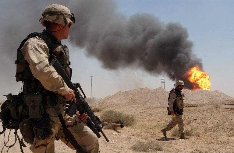 US Navy 030402-N-5362A-004 U.S. Army Sgt. Mark Phiffer stands guard duty near a burning oil well in the Rumaylah Oil Fields in Southern Iraq-768x504